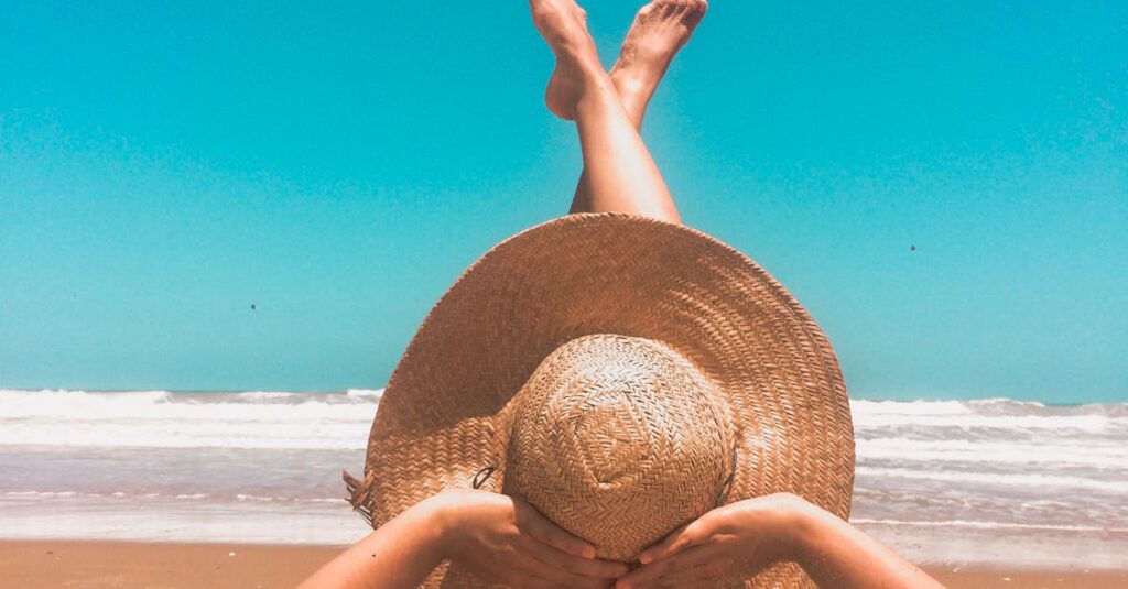 A woman in a straw hat relaxes on a sunny beach, enjoying the clear blue sky and ocean waves.