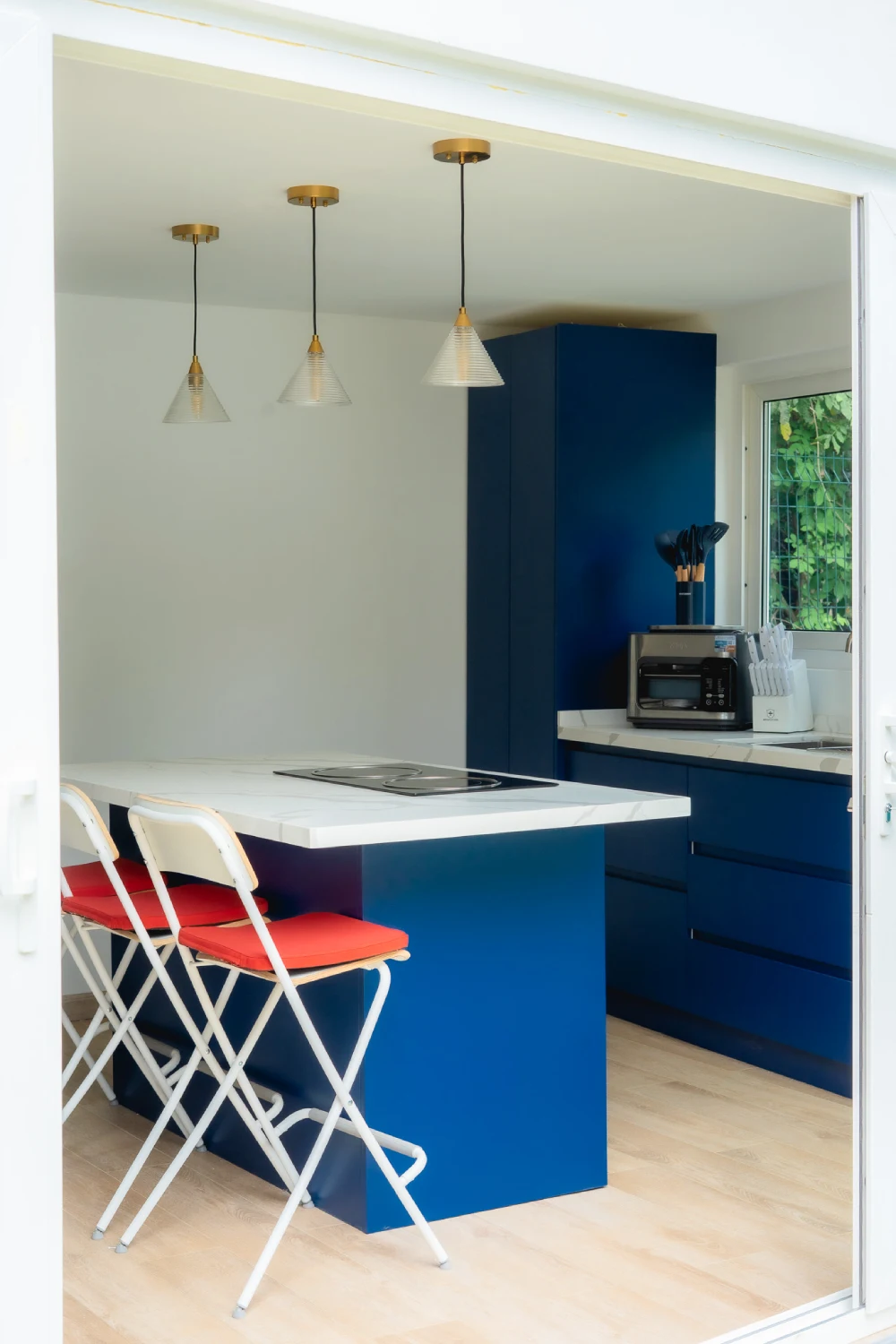 The kitchen offers the blue center island with the stovetop, the breakfast bar high chairs, and the pendant lights.