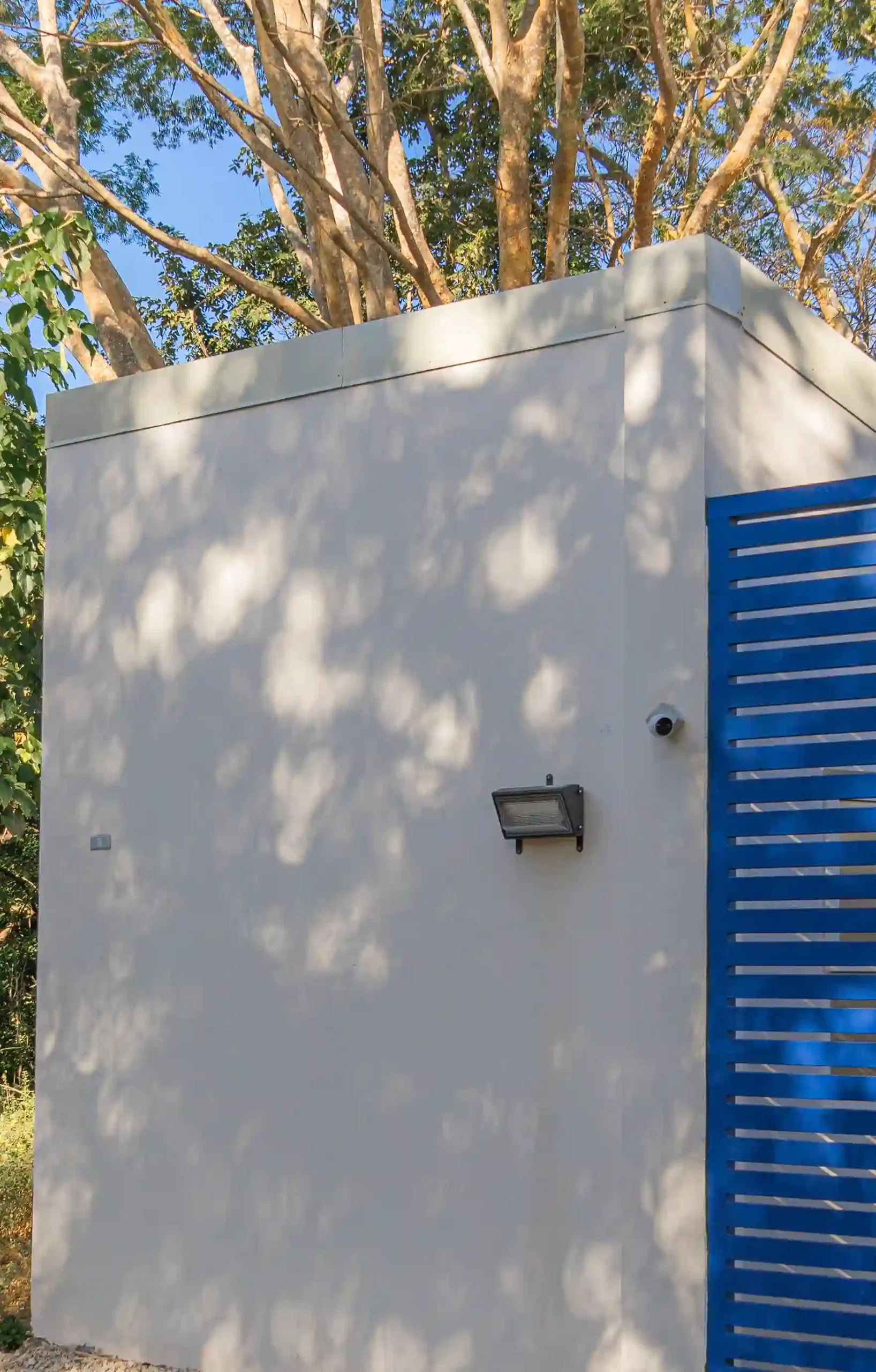 Security system featuring a CCTV camera and outdoor lighting on the white wall next to the blue T Loft gate.