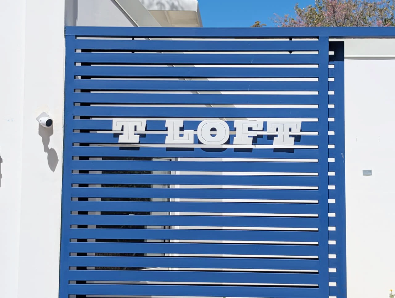 Blue T Loft gate featuring the white logo and a keypad access control system at the pedestrian entrance.