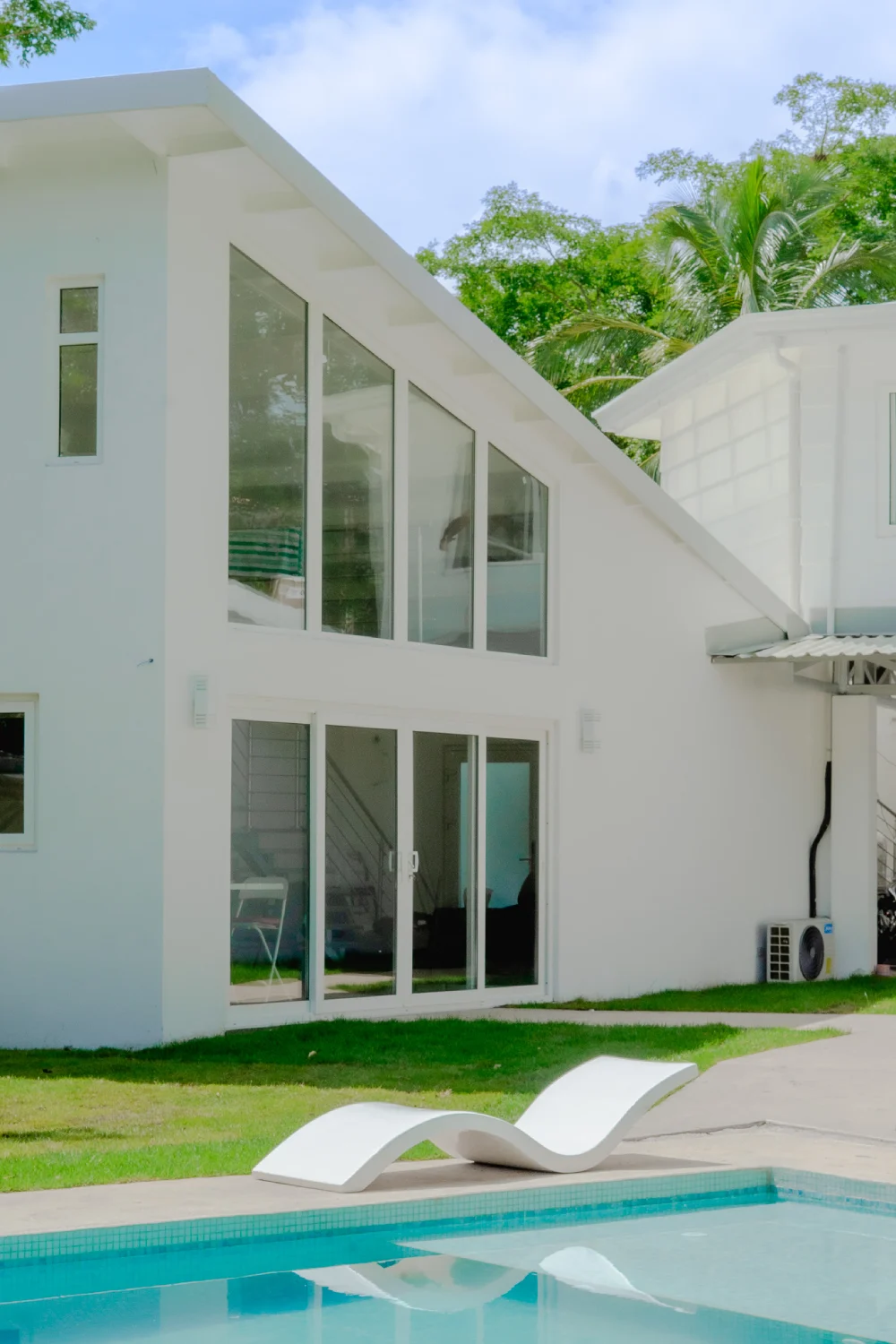 Open-plan architecture with large glass windows and designer lounger facing turquoise pool