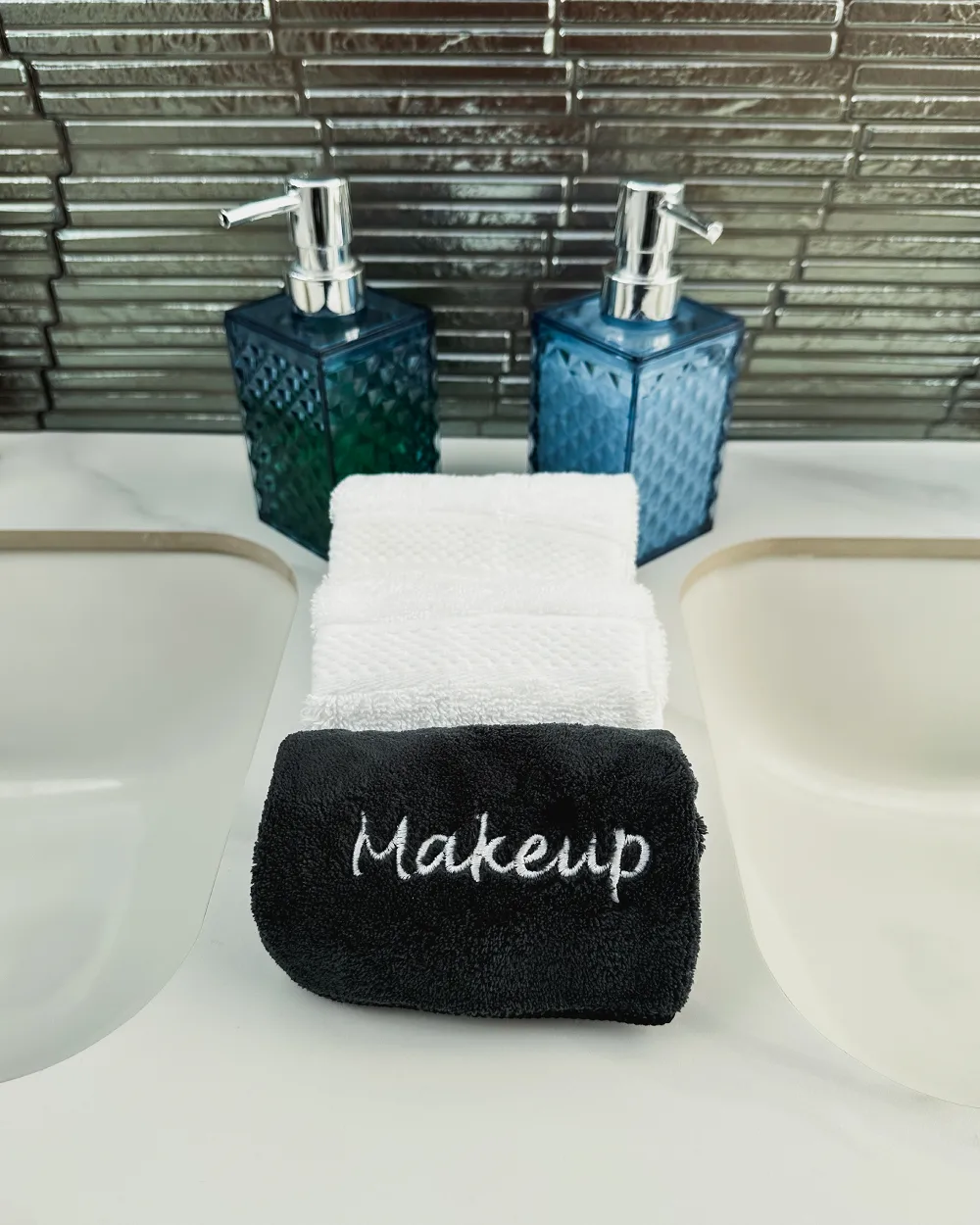 Blue soap dispensers and white towels with a black makeup towel on a double vanity.