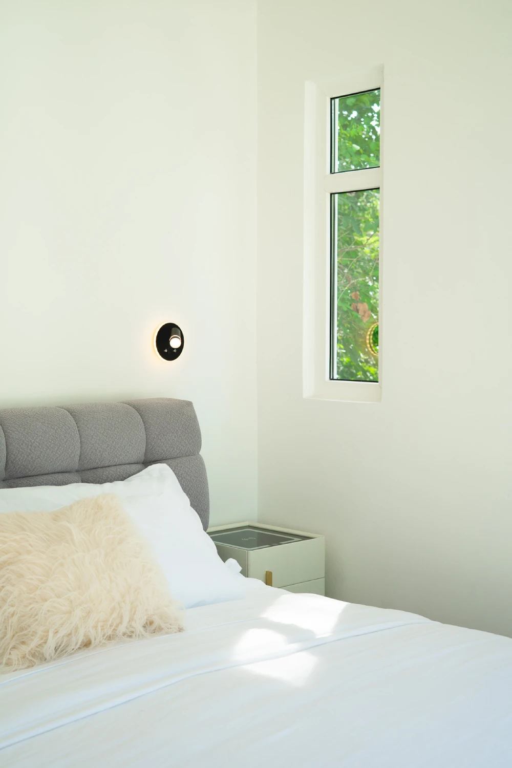 Circular wall lamp with warm light and window overlooking the garden.